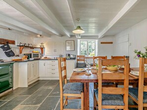 A kitchen with white cabinets, a green stove, and a dining area with a wooden table and chairs. - 3 Bed in Truro (oc-90716) (Philleigh)