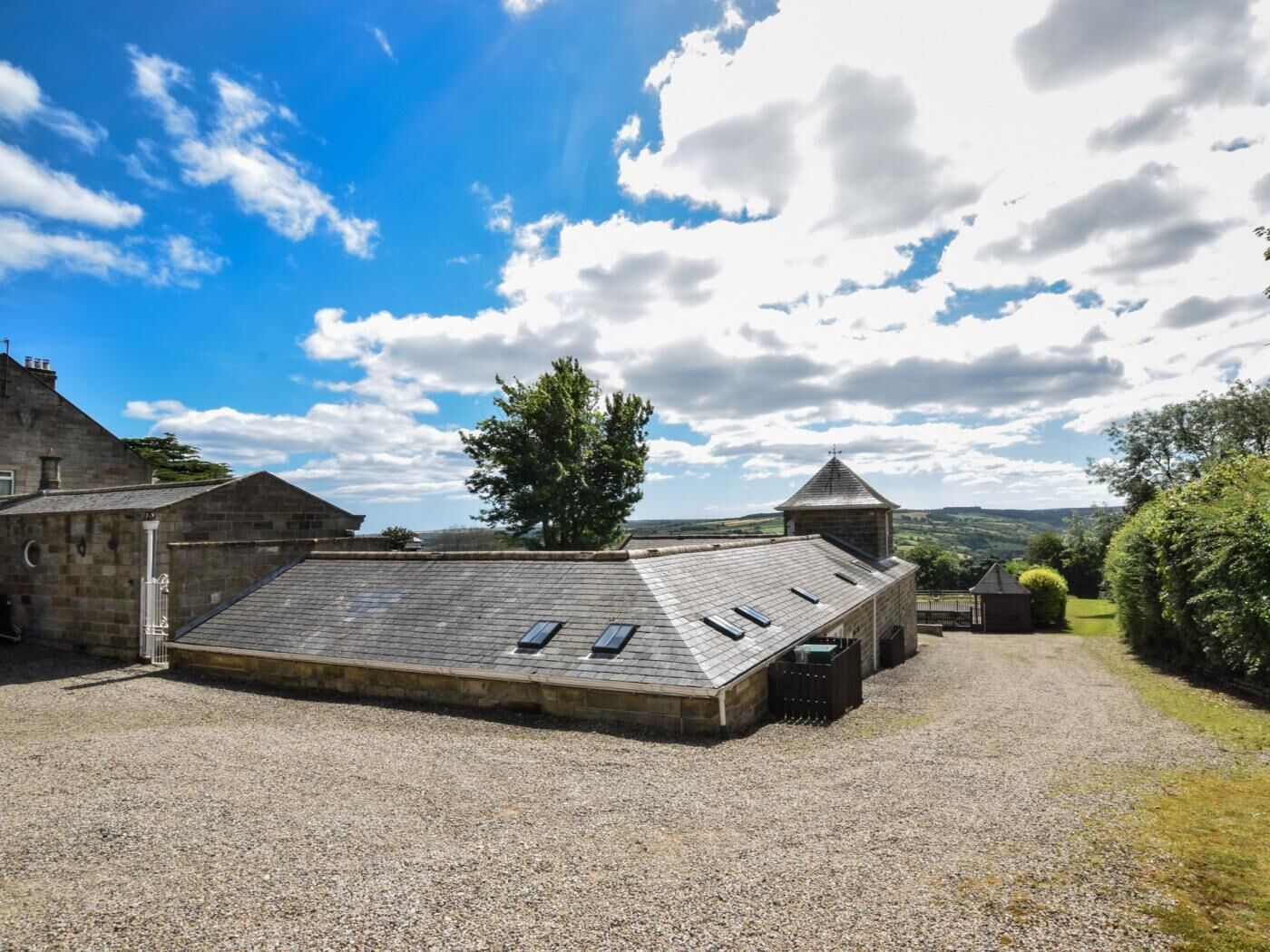 A building with a sloped roof, a gravel driveway, and a view of the countryside.