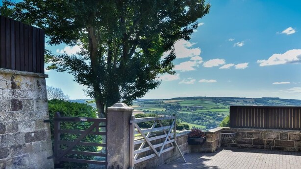 A paved entrance with a wooden gate, a stone wall, and a view of rolling hills. - 3 Bed in Whitby (oc-90809) (Aislaby)