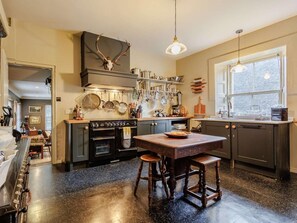 A kitchen with a central island, a stove, and various kitchen utensils on the wall. - 5 Bed in Dunkeld (oc-90844) (Birnam)