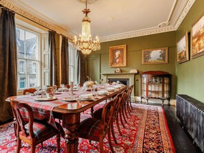 A formal dining room with a long table set for a meal, flanked by chairs, a chandelier, and a fireplace. - 5 Bed in Dunkeld (oc-90844) (Birnam)