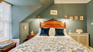 Une chambre avec un plafond en pente, un grand lit recouvert d’une couvre-lit à motifs floraux, une tête de lit en bois et un lustre.