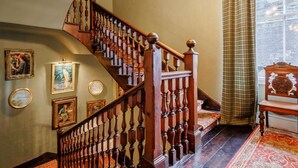 Un escalier en bois avec une balustrade, un tapis à motifs et des œuvres d’art encadrées accrochées aux murs.