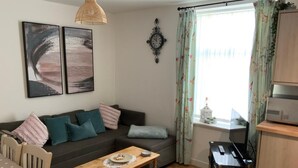 Een woonkamer met een bank, een salontafel, een eettafel en een keuken met een fornuis.