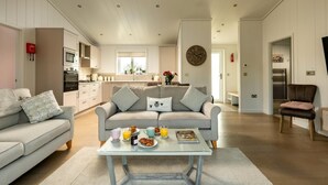 A modern living room with a sofa, coffee table, and a dining area with breakfast items. - 2 Bed in Castle Douglas (oc-90821) (Auchencairn)