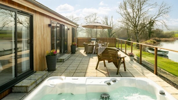 A patio with a hot tub, outdoor furniture, and a view of a lake. - 2 Bed in Castle Douglas (oc-90821) (Auchencairn)