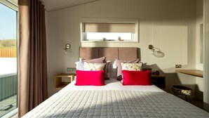A bedroom with a large bed, a nightstand, a bedside table, a window with curtains, a headboard, a wall-mounted shelf, and a wall-mounted lamp. - 2 Bed in Castle Douglas (oc-90821) (Auchencairn)