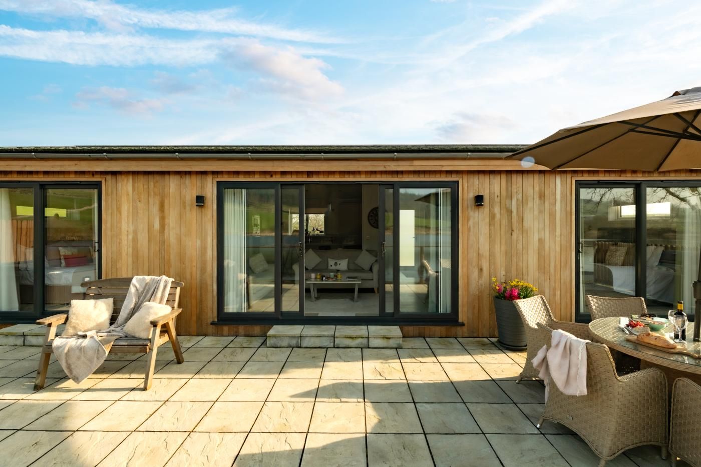 Ein modernes Gebäude mit Holzfassade, großen Schiebeglastüren und einer Terrasse mit Gartenmöbeln.