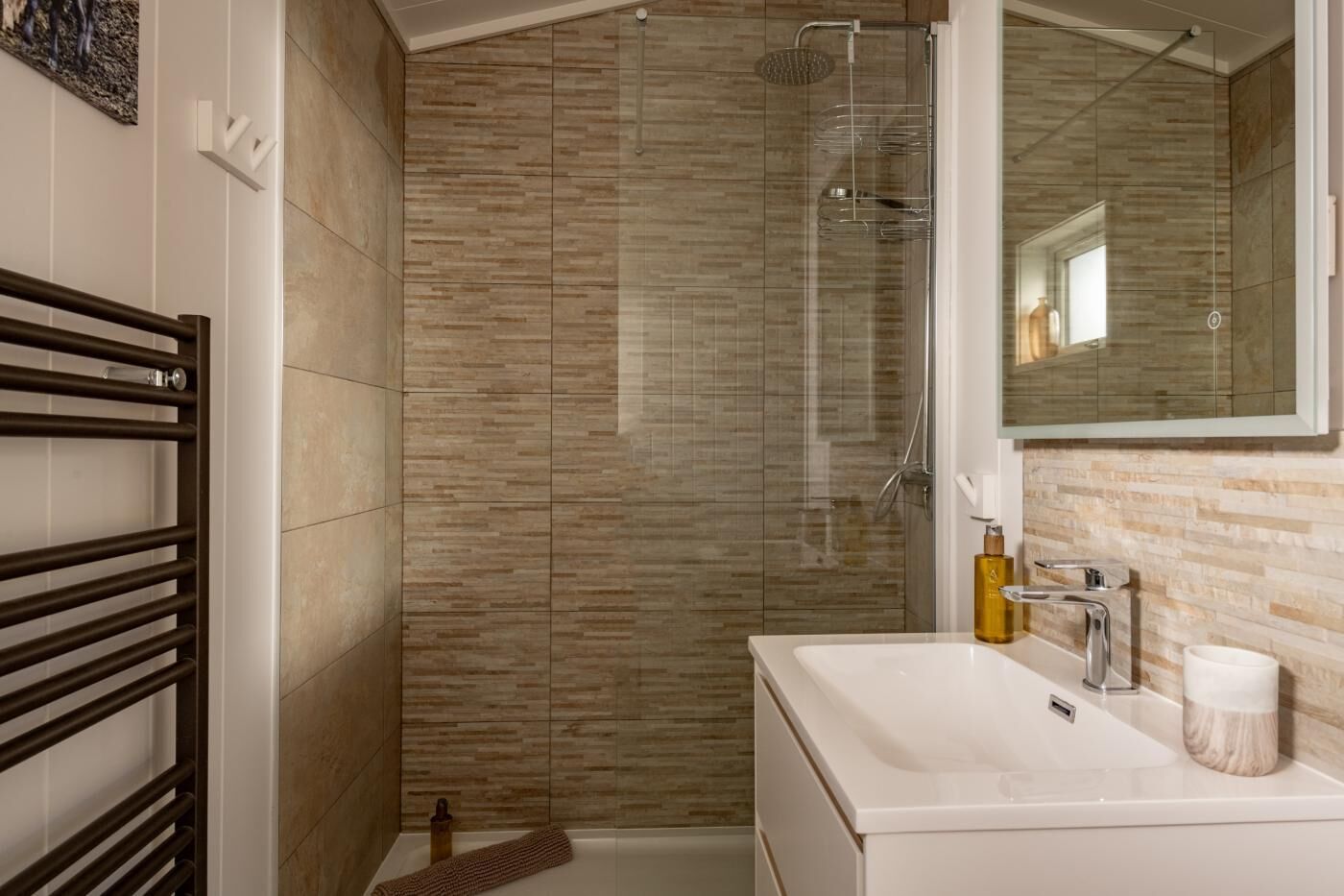 A bathroom with a glass shower enclosure, a white sink, and a towel rack.