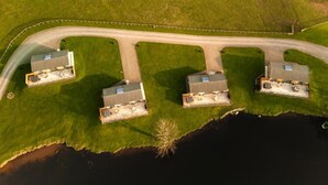 An aerial view of a property with four buildings, a curved road, and a body of water. - 2 Bed in Castle Douglas (oc-90821) (Auchencairn)