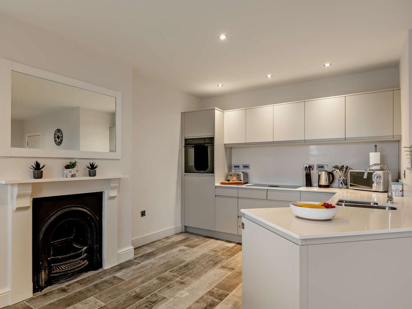A modern kitchen with white cabinetry, a built-in oven, a microwave, and a central island with a bowl of fruit.