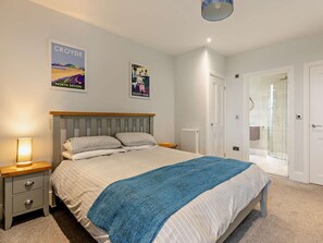 Ein Schlafzimmer mit einem Bett, Nachttischen, einer Nachttischlampe, einer blauen Tagesdecke und zwei Bildern an der Wand.
