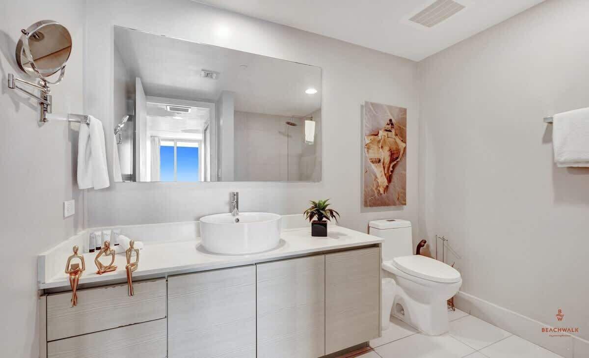 A modern bathroom with a large mirror, a sink, a toilet, and a shower.