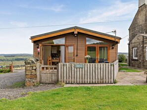 A small wooden building with a stone wall entrance, a wooden fence, and a sign indicating it is a holiday home.