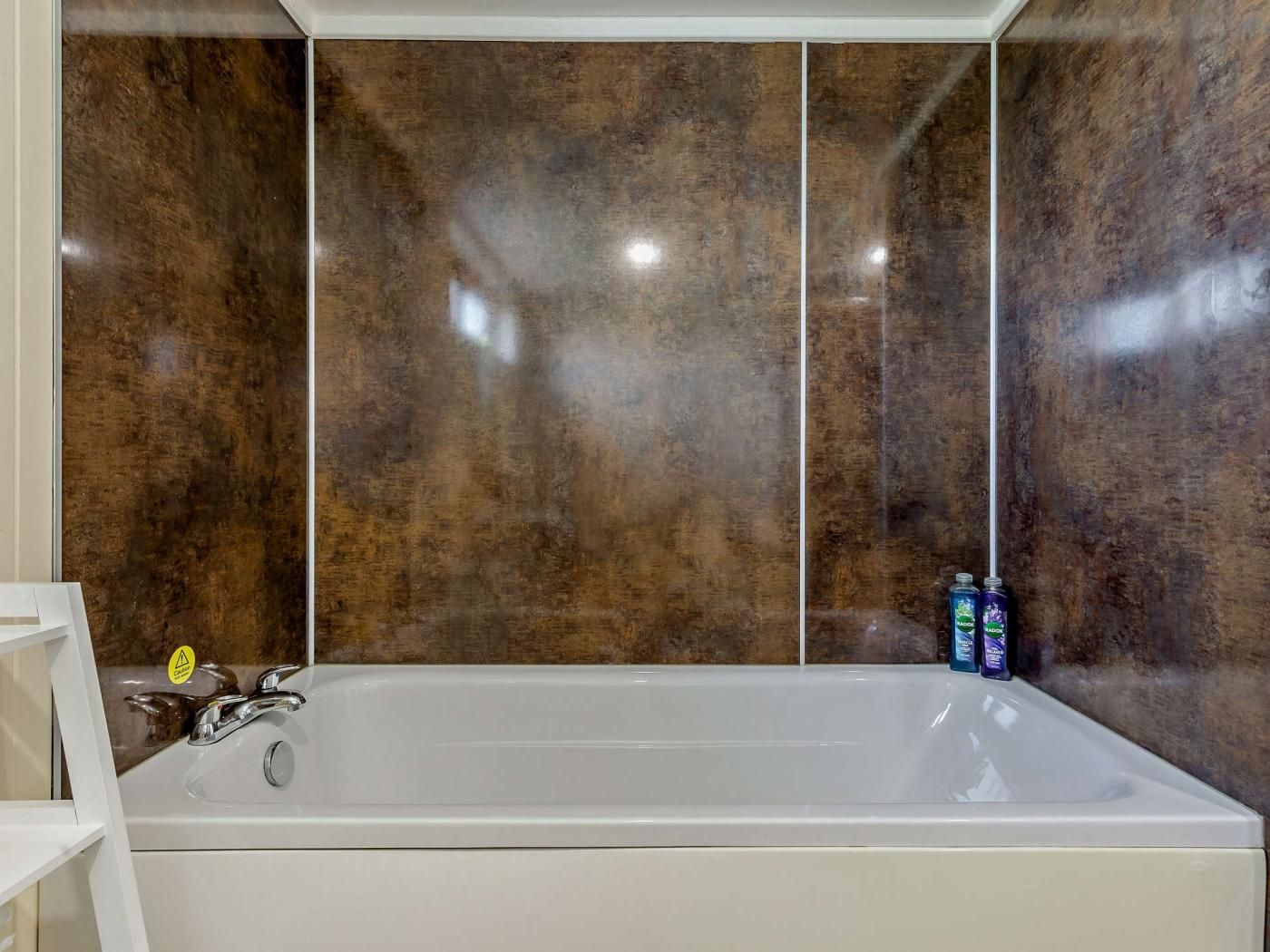 Une salle de bain avec une grande baignoire, un lavabo blanc et un miroir. Deux bouteilles sont posées sur le bord de la baignoire.
