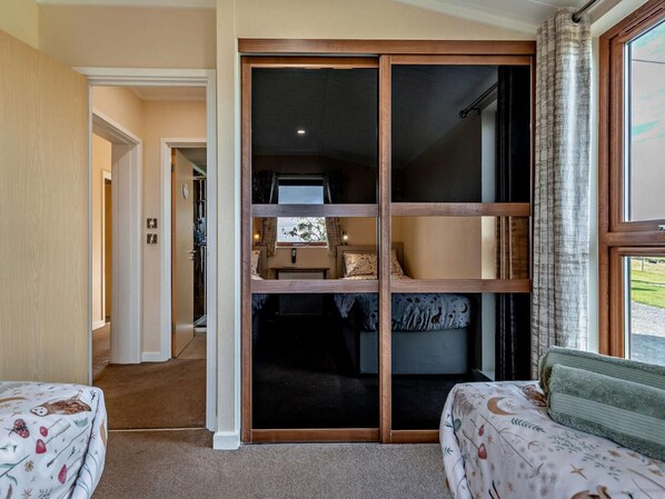A bedroom with a sliding door closet, a bed with patterned bedding, and a view of the outdoors through a window.