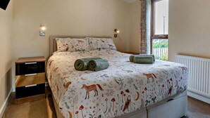 A bedroom with a bed, bedside tables, a window with curtains, and a radiator.
