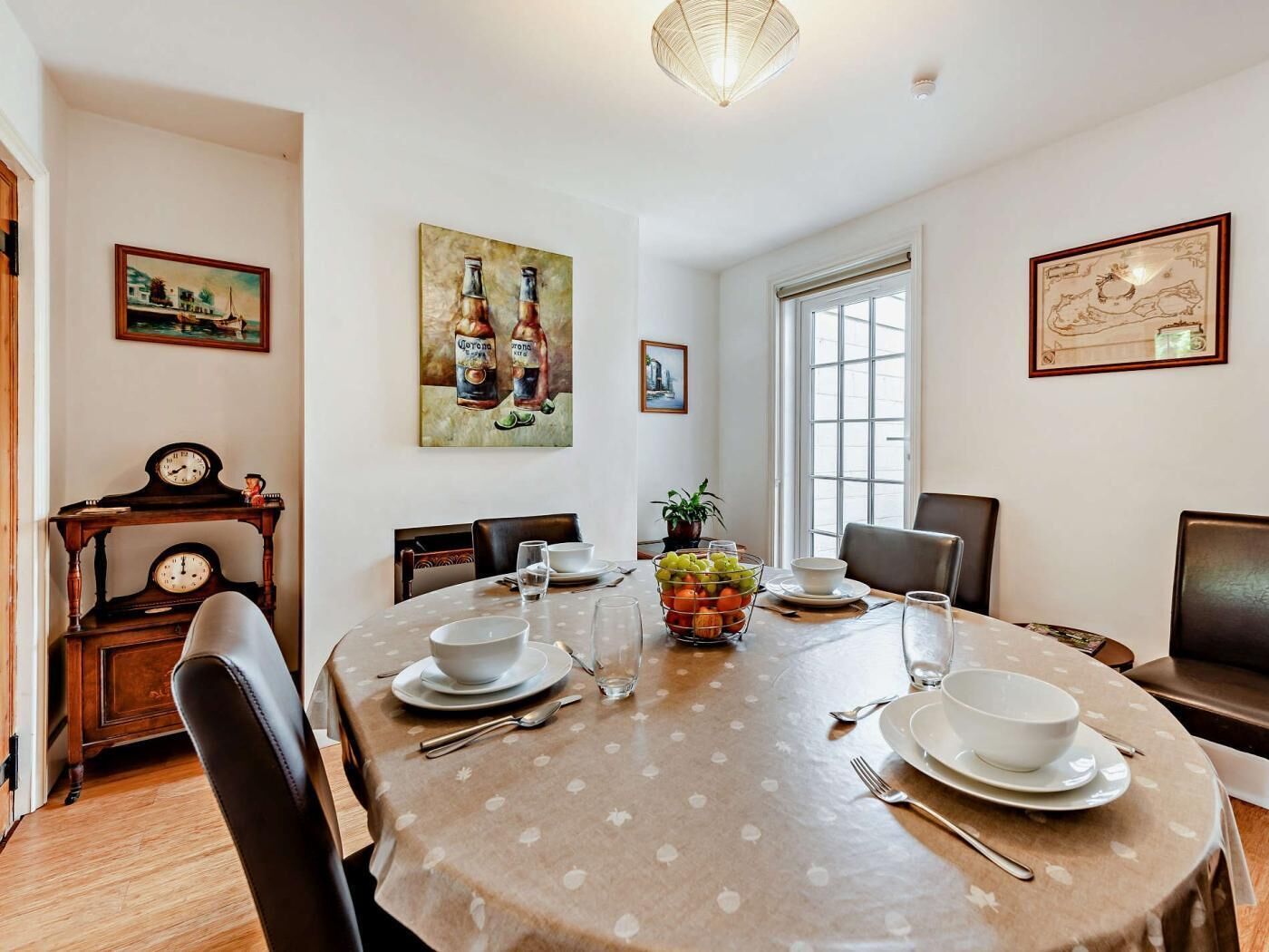 A dining room with a round table, chairs, a clock, and artwork on the walls.