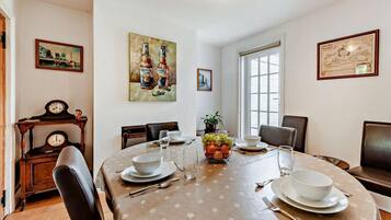 A dining room with a round table, chairs, a clock, and artwork on the walls.