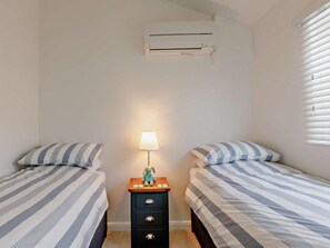 A bedroom with two single beds, a bedside table with a lamp, and an air conditioning unit. - 2 Bed in Brixham (oc-90912) (Brixham)