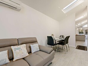 Una sala moderna con sofá, mesa de comedor, sillas y una cocina al fondo.
