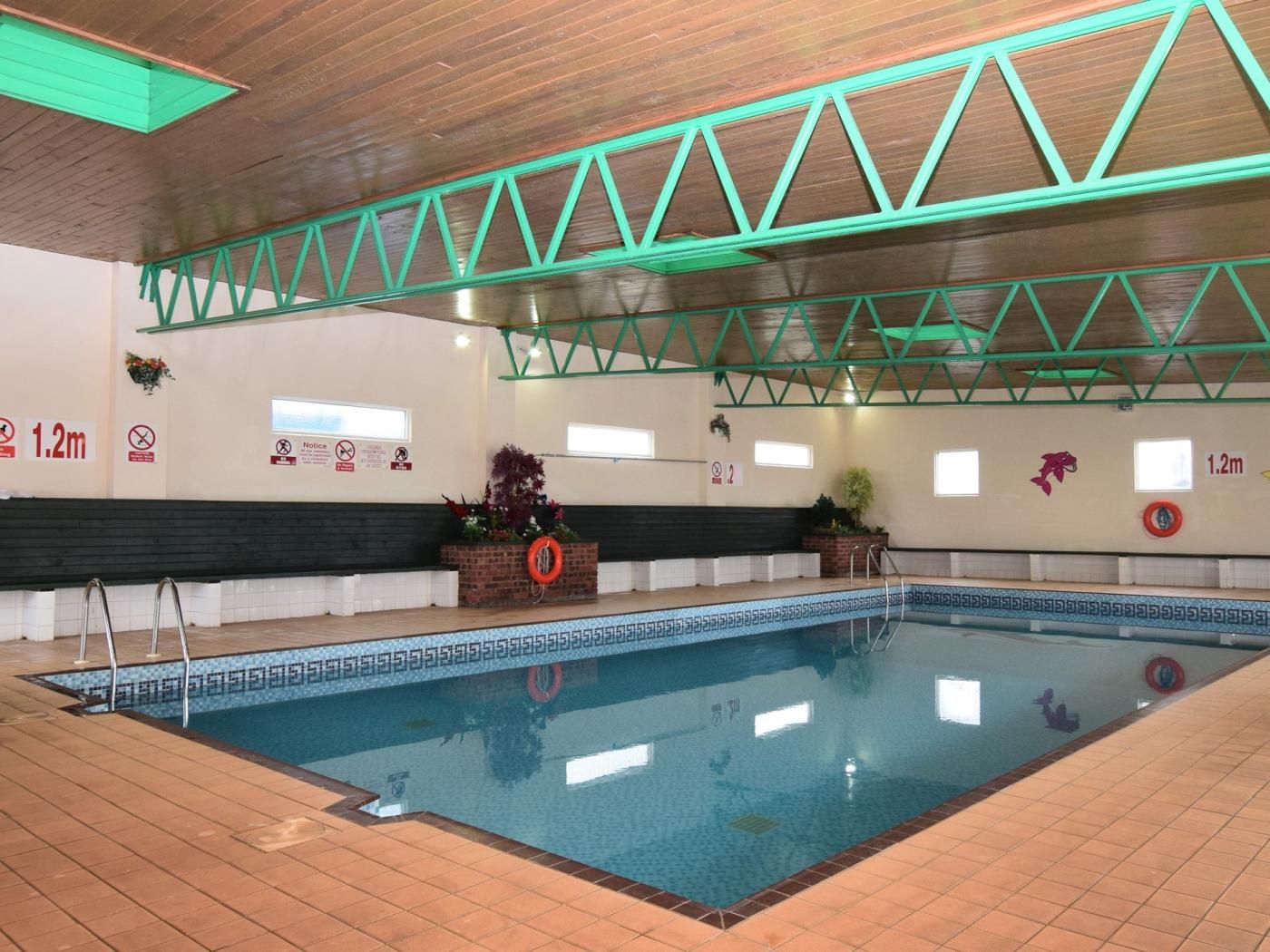 An indoor swimming pool with a wooden ceiling, green structural beams, and tiled flooring.