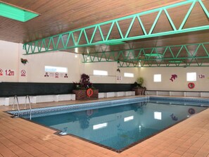 Una piscina interior con techo de madera, vigas estructurales verdes y suelo de baldosas.