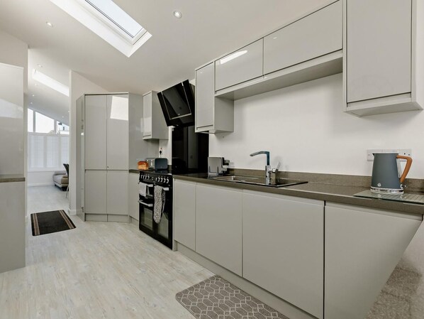 A modern kitchen with a built-in oven, a sink, and a kettle on the countertop. - 2 Bed in Brixham (oc-90912) (Brixham)