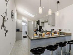 A modern kitchen with a central island, bar stools, pendant lighting, and a visible refrigerator. - 2 Bed in Brixham (oc-90912) (Brixham)