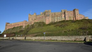Eine große, historische Burg auf einem Hügel mit einem befestigten Parkplatz davor.