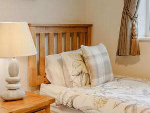 A bedroom with a wooden headboard, a bedside table with a lamp, and a floral bedspread. - 2 Bed in Bamburgh (oc-90879) (Bamburgh)
