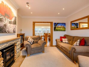 A cozy living room with a fireplace, two sofas, and a dining area in the background. - 2 Bed in Bamburgh (oc-90879) (Bamburgh)