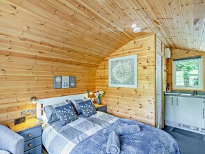 A wooden cabin bedroom with a bed, bedside table, and a window. - 1 Bed in Church Stretton (oc-90929) (All Stretton)