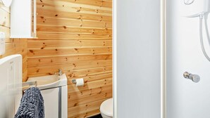 Et badeværelse med vægge af træpaneler, en hvid vask, toilet og bruseområde.