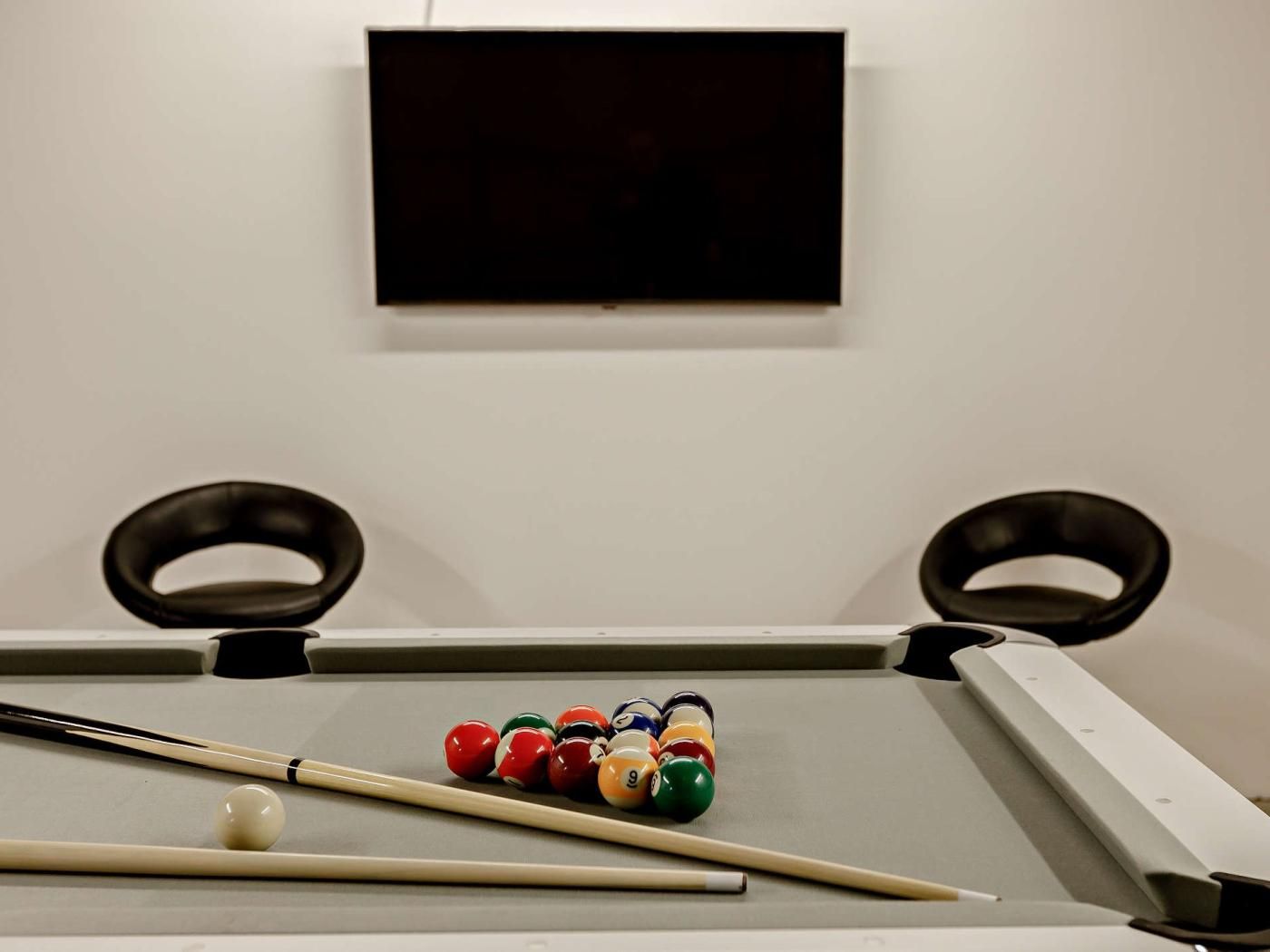 A pool table with balls and cues, a television mounted on the wall, and two rings on the table's sides.