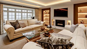 Una sala de estar moderna con un sofá color beige, una mesa de centro de vidrio, una chimenea y un televisor montado en la pared.