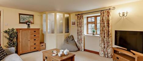 A cozy living room with a sofa, a wooden coffee table, a TV stand, and a window with curtains.