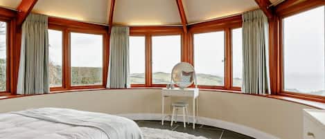 A bedroom with a bed, a desk with a mirror, and large windows with curtains.