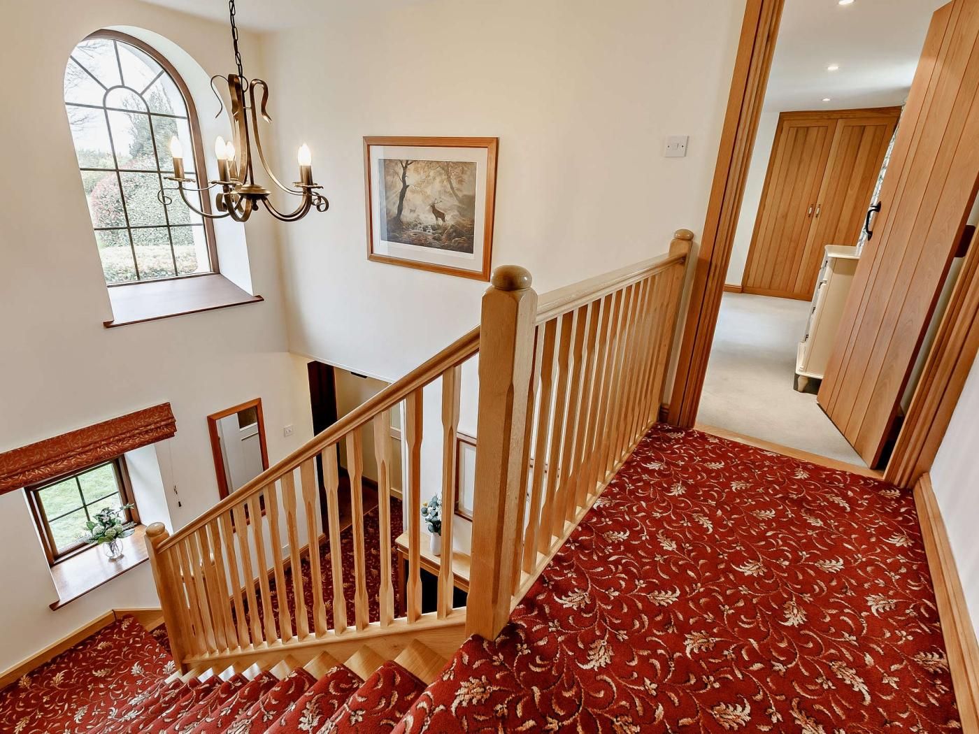 A staircase with a wooden railing leading to a landing, a chandelier, and a framed picture on the wall.