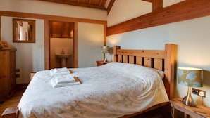 Un dormitorio con estructura de madera, una cama, una mesita de noche con lámpara, un espejo y un aparador de madera.