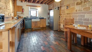 Una cocina rústica con vigas de madera, pared de piedra, una mesa de comedor de madera y un refrigerador.