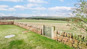 Un muro de piedra, una zona cubierta de césped y una vista distante de colinas.