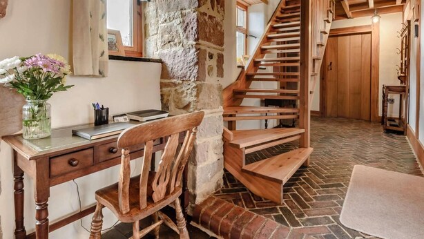 Un interior rústico con pared de piedra, escritorio de madera, silla y escalera en espiral de madera.