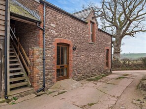 A stone building with a wooden staircase leading to a door, a large tree in the background, and a clear sky. - 2 Bed in Brecon (oc-91085) (Llangorse)