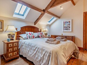 A bedroom with a sloped ceiling, wooden beams, a bed with a headboard, bedside tables, lamps, a dresser, and a skylight. - 2 Bed in Brecon (oc-91085) (Llangorse)