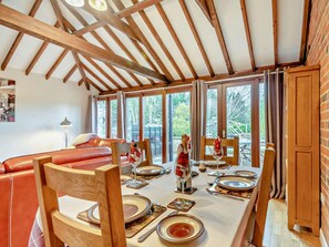 A dining area with a long table set for four, wooden chairs, and a view of the outdoors through large windows. - 2 Bed in Lincoln (oc-91059) (Ashby de la Launde)