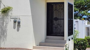 A modern building with a white facade, a black decorative door, and a small set of steps leading to the entrance. - Apto nuevo - Comunidad segura cerca de SJO y SJ (Heredia)