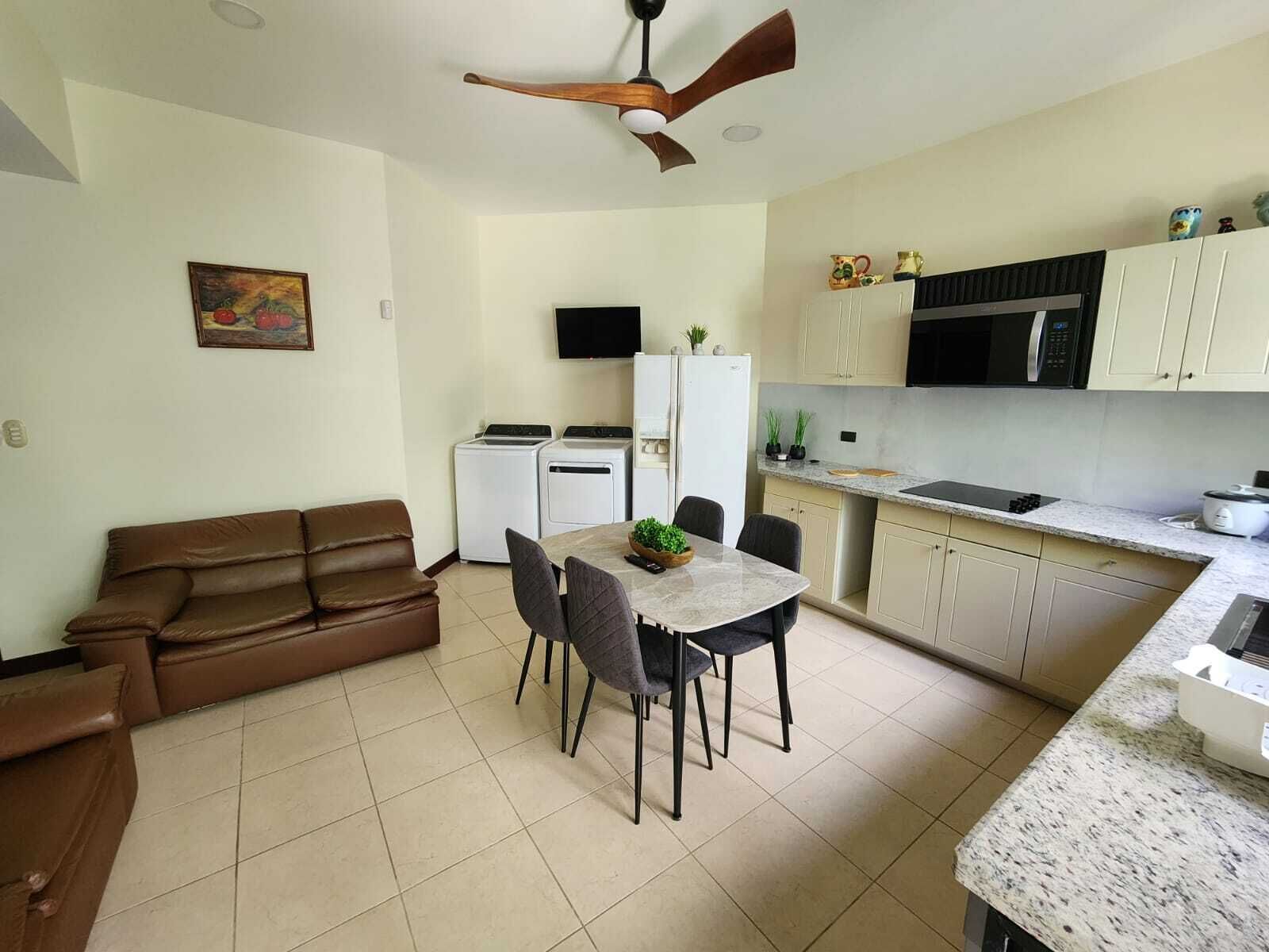 A compact kitchen with a dining area, a ceiling fan, and a sofa.