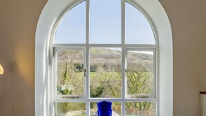 A large arched window with a view of a rural landscape. - 6 Bed in Abergele (oc-91054) (Llanddulas)