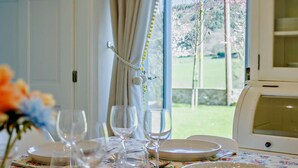 A dining table set with plates, glasses, and cutlery, a window with curtains, and a view of greenery outside. - 6 Bed in Abergele (oc-91054) (Llanddulas)